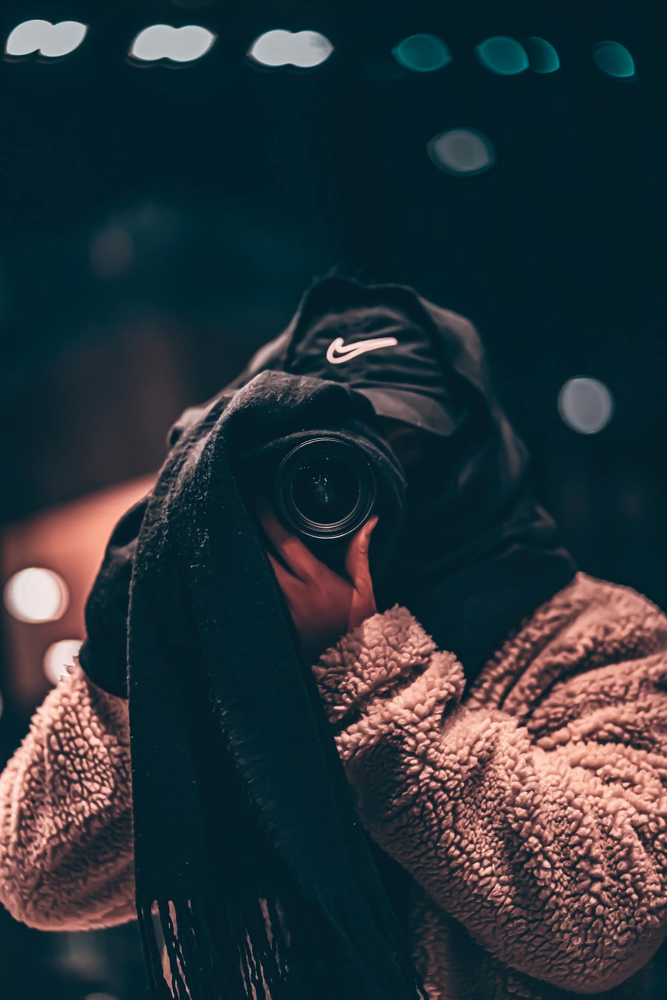 Unrecognizable person wearing hooded clothes and hiding face behind black scarf taking photo on professional camera on blurred background